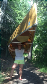 Tiara carrying a canoe overhead on a wooded trail